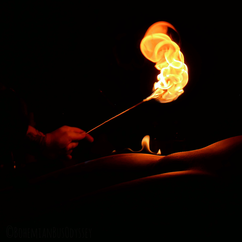 A photo I took showing a golden flame being manipulated over a naked body.  The photo is dark, close up, and only illuminated by the flame.