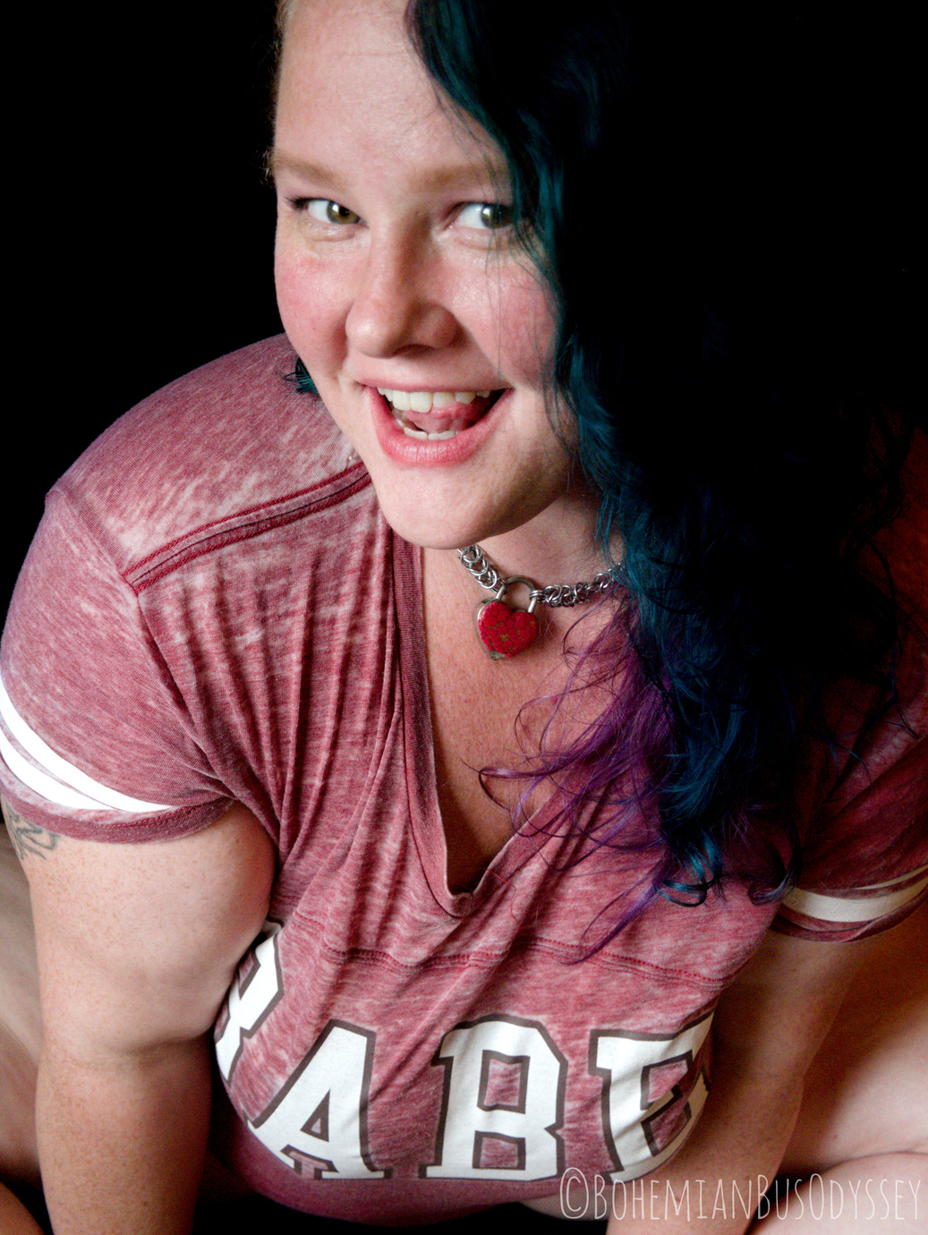 A woman with blue hair and a big happy smile wearing a pink shirt. 